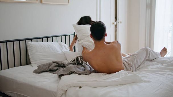 笑う配偶者は寝室で戦っている枕. 面白い愛のカップルが一緒に朝を過ごすアクティブなゲームに参加しました. 居心地の良いアパートのインテリアで寝具製品で遊び心のあるエネルギー愛好家  - 写真・画像