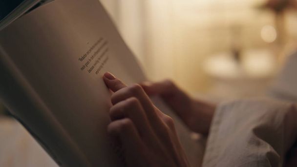 Closeup handen houden boek binnen. Een glimlachende vredige vrouw die haar favoriete roman leest op een weekendvakantie avond. Een kalme studente die thuis informatie leert. Bladzijden met vingerwijzingen - Foto, afbeelding
