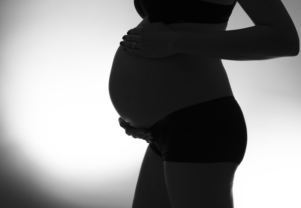 A Black and white silhouette of a woman's pregnant belly - Zdjęcie, obraz