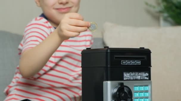 A little boy puts a coin into a safe piggy bank. Financial literacy for children - Footage, Video