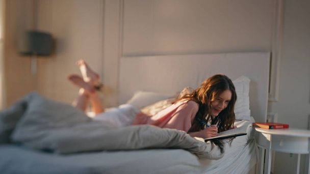 Przemyślana kobieta pisząca dziennik rano. Marzycielski nastolatek dzieli się uczuciami w notatniku leżącym na łóżku. Romantyczna szczęśliwa dziewczyna korzystająca z dnia planowania organizatora. Koncepcja wyobraźni inspiracji. - Zdjęcie, obraz