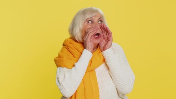 Keep my secrets, silence. Senior old woman whisper news rumors holding hands near mouth, share gossip, quiet. Elderly grandmother pensioner telling interesting confidential story on yellow background - Footage, Video