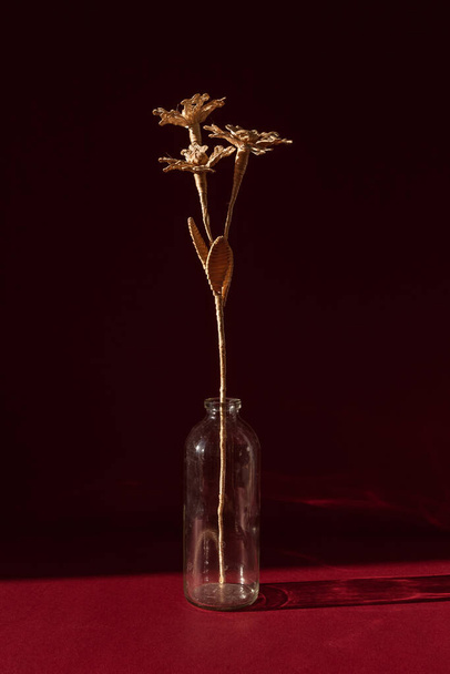 Kırmızı arka planda samandan yapılmış bir buket çiçekli cam bir vazo. Çiçek güneş tarafından aydınlatılır. Küçük alan derinliği.  - Fotoğraf, Görsel