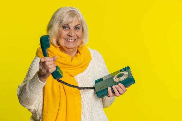 電話してくれ。 80年代の有線ランドラインのヴィンテージ電話,会話の広告提案,オンラインショッピング,ホットラインで話す高齢女性. 黄色の背景に成熟したおばあちゃん - 写真・画像