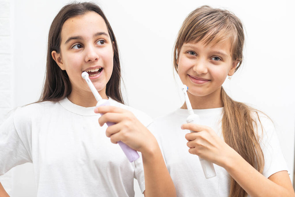 Portret van twee mooie meisjes met een perfecte glimlach die tandenborstels vasthoudt. Kindertandheelkundige verzorging, mondhygiëne concept. Hoge kwaliteit foto - Foto, afbeelding