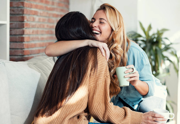 Выстрел из двух милых улыбающихся женщин, обнимающих друг друга во время разговора, сидящих на диване в гостиной дома. - Фото, изображение