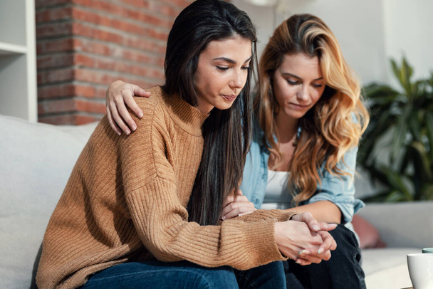 Shot of pretty young woman supporting and comforting her sad friend while sitting on the sofa at home. - Foto, afbeelding