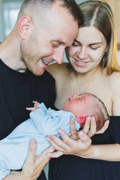Happy young parents hold their newborn son in their arms. Smiling happy couple hugging their newborn baby. One day for a newborn baby. - Photo, Image