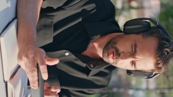 A fejhallgatós fickó mobilt gépel, élvezi a zenét a parkasztalnál, vertikálisan közelről. Relaxált hanggyártó remix létrehozása okostelefon alkalmazással a városban. Latin szabadúszó SMS mobiltelefon a munkahelyen  - Felvétel, videó