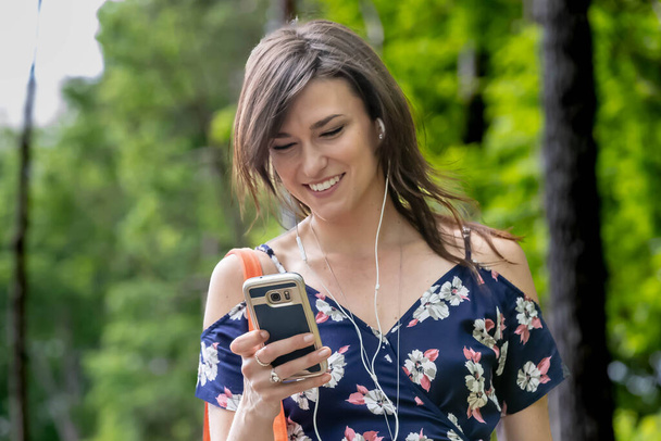 Une étudiante brune, absorbée par son téléphone portable, se dirige rapidement vers la classe, naviguant harmonieusement dans la vie du campus - Photo, image