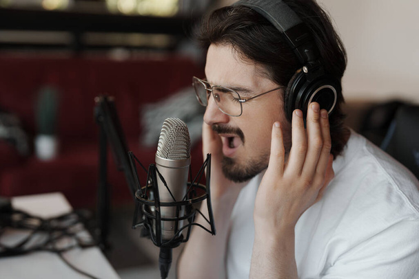 Ένας αρσενικός τραγουδιστής παίζει παθιασμένα σε ένα μικρόφωνο στούντιο, κατέγραψε το μεσαίο τραγούδι κατά τη διάρκεια μιας ηχογράφησης. - Φωτογραφία, εικόνα
