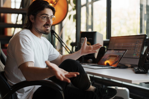 Музыкальный продюсер в студии, объясняя концепцию жестом руками, среди профессионального записывающего оборудования - Фото, изображение
