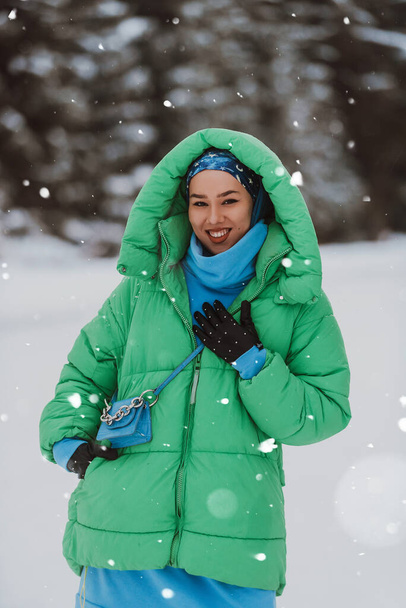 In den atemberaubenden schneebedeckten Bergen posiert eine schöne Frau in Hijab und grünem Sakko mit Anmut und verbindet Bescheidenheit und Stil in der Winterlandschaft.  - Foto, Bild