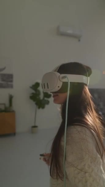Utilizando gafas de realidad virtual 3D, una hermosa joven juega un juego virtual en su casa. Imágenes de alta calidad 4k - Imágenes, Vídeo