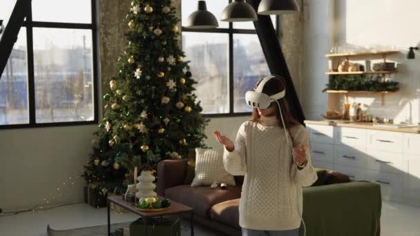 Eine schöne junge Frau justiert ein Virtual-Reality-Headset in der Nähe eines Weihnachtsbaums. Hochwertiges 4k Filmmaterial - Filmmaterial, Video