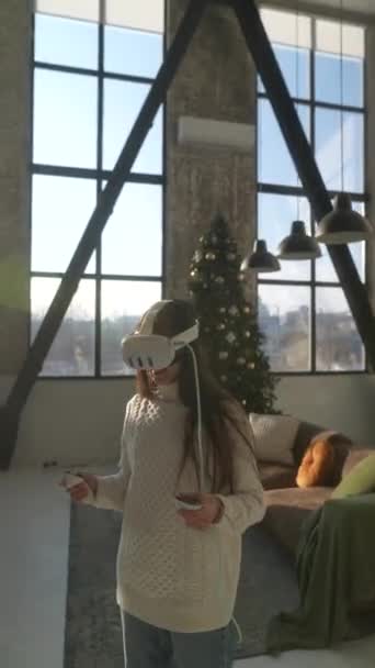 Dans un appartement de Noël lumineux, une jeune femme animée arbore un casque de réalité virtuelle. Images 4k de haute qualité - Séquence, vidéo