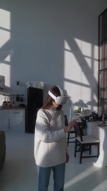 Gösterişli, modern bir dairede, genç bir bayan, açık renk giyinmiş bir şekilde sanal gerçeklik kulaklığı takıyor. Yüksek kalite 4k görüntü - Video, Çekim