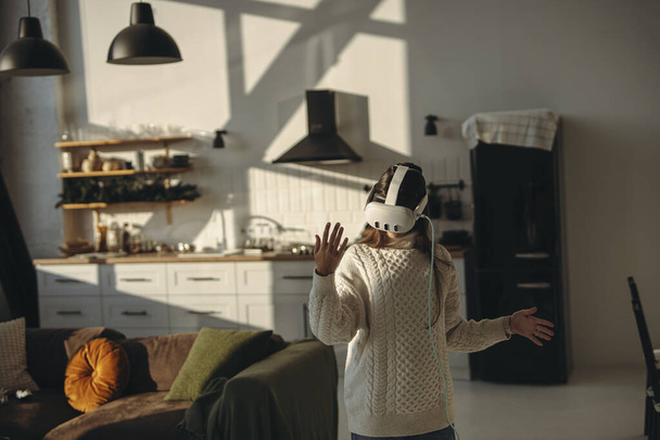 Scavando in un gioco online, una bella giovane donna utilizza un auricolare realtà virtuale a casa. Foto di alta qualità - Foto, immagini
