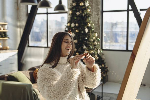 Avec un esprit joyeux, une jeune femme brillante portant un masque de renne de Noël illumine l'appartement avec son sourire. Photo de haute qualité - Photo, image
