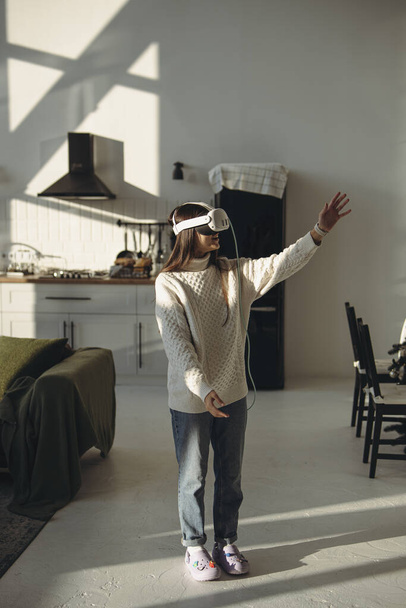 Jugando un juego en línea, una encantadora joven disfruta de sus auriculares VR en el apartamento. Foto de alta calidad - Foto, Imagen