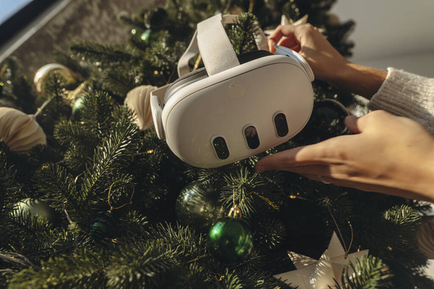 Met een kerstboom op de achtergrond, houdt een meisje een virtual reality headset vast. Hoge kwaliteit foto - Foto, afbeelding