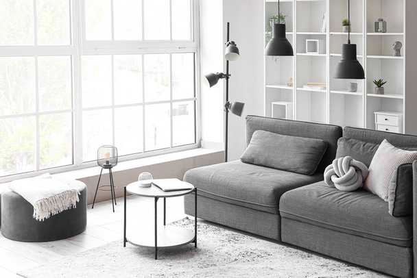 Інтер'єр світлої вітальні з затишним сірим диваном і журнальним столиком біля великого вікна
 - Фото, зображення