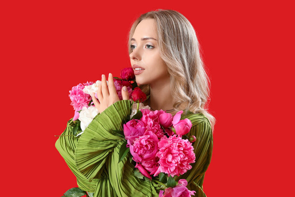Mujer joven con hermosas flores de peonía sobre fondo rojo - Foto, imagen