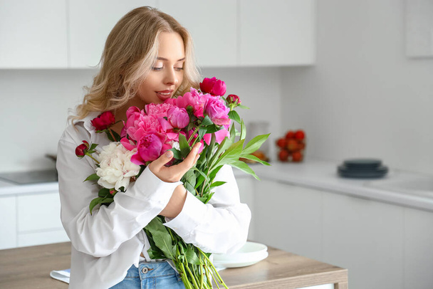 Mujer joven con flores de peonía en la cocina - Foto, Imagen