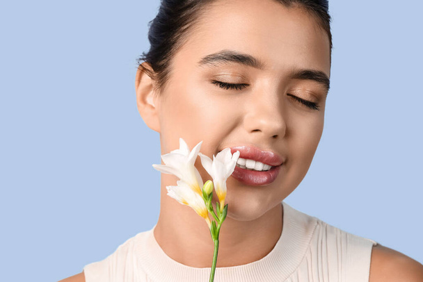 Young woman with beautiful lips and flower on blue background, closeup - Photo, Image