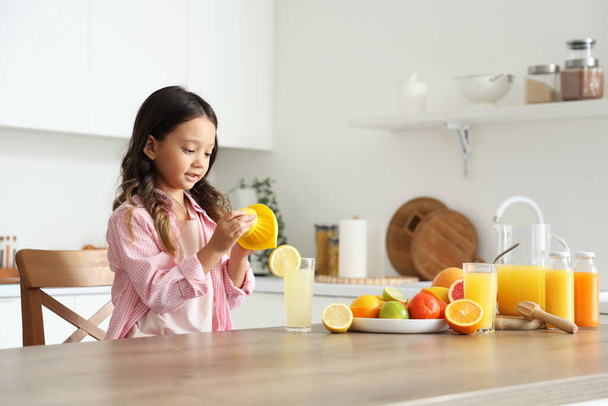 キッチンのテーブルで新鮮な柑橘類ジュースを作る小さなアジアの少女 - 写真・画像
