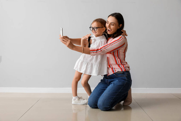 Красива мати і її мила маленька дочка з мобільним телефоном бере селфі біля сірої стіни - Фото, зображення
