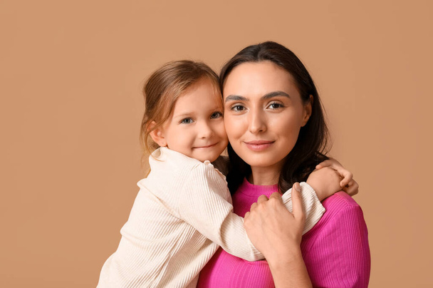 Piękna matka przytula się ze swoją uroczą córeczką na brązowym tle - Zdjęcie, obraz