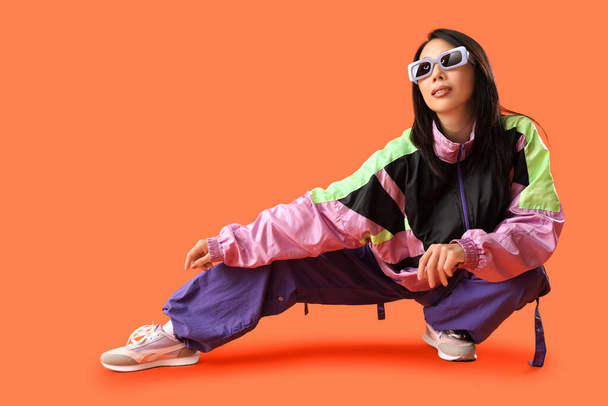 Bella donna asiatica elegante in occhiali da sole in posa su sfondo arancione - Foto, immagini