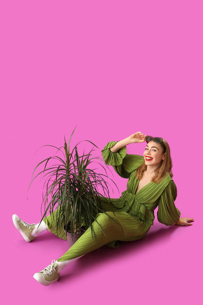 Beautiful young stylish woman in sunglasses with houseplant on purple background - Photo, Image