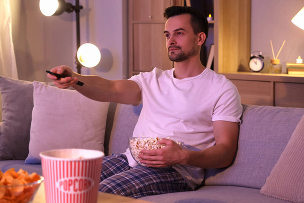 Nuori mies, jolla on popcornia, katselee televisiota kotona illalla - Valokuva, kuva