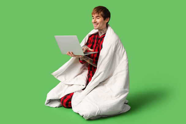 Hezký mladý muž s dekou pomocí notebooku na zeleném pozadí - Fotografie, Obrázek