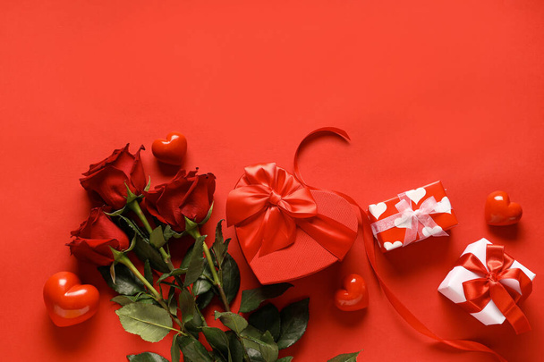 Boeket van prachtige rozen met harten en geschenkdozen op rode achtergrond. Valentijnsdag - Foto, afbeelding