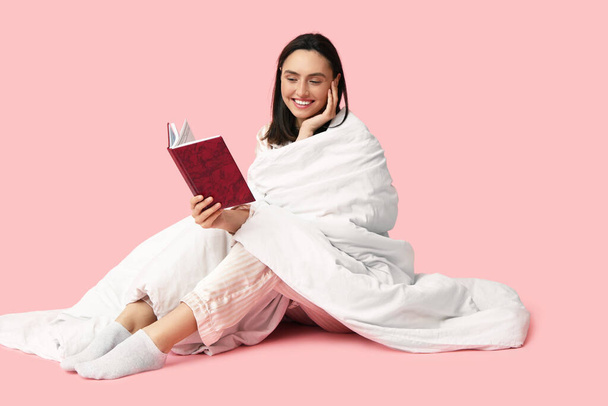 Όμορφη νεαρή γυναίκα με κουβέρτα βιβλίο ανάγνωσης σε ροζ φόντο - Φωτογραφία, εικόνα