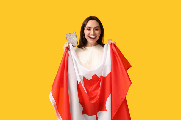 Όμορφη νεαρή γυναίκα με σημαία του Καναδά και διαβατήριο σε κίτρινο φόντο. Έννοια μετανάστευσης - Φωτογραφία, εικόνα
