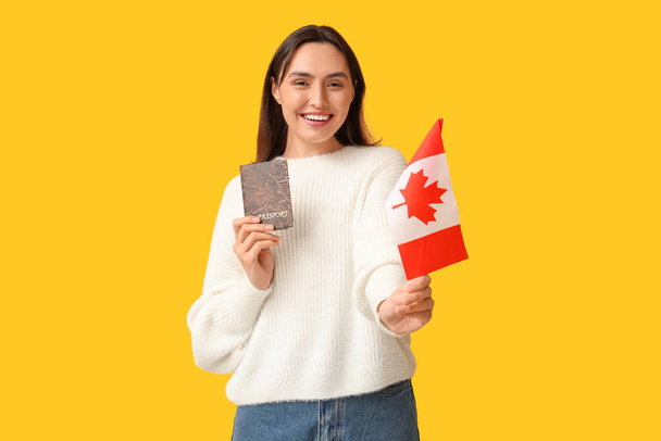 Ładna młoda kobieta z flagą Kanady i paszportem na żółtym tle. Koncepcja imigracji - Zdjęcie, obraz