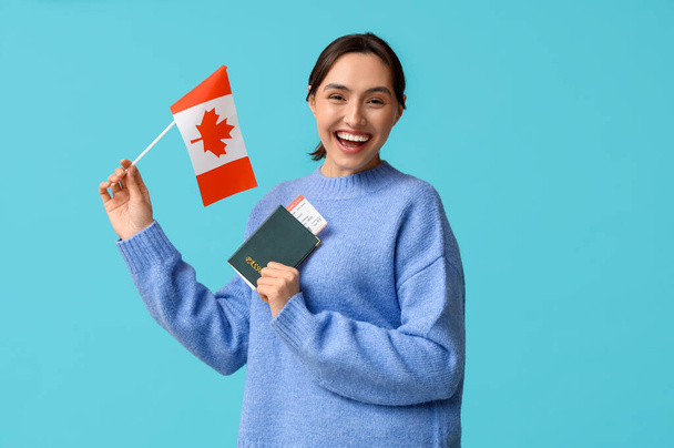 Όμορφη νεαρή γυναίκα με σημαία του Καναδά και διαβατήριο σε μπλε φόντο. Έννοια μετανάστευσης - Φωτογραφία, εικόνα