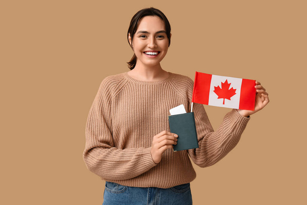 Mujer joven y bonita con bandera de Canadá y pasaporte sobre fondo beige. Concepto de inmigración - Foto, Imagen