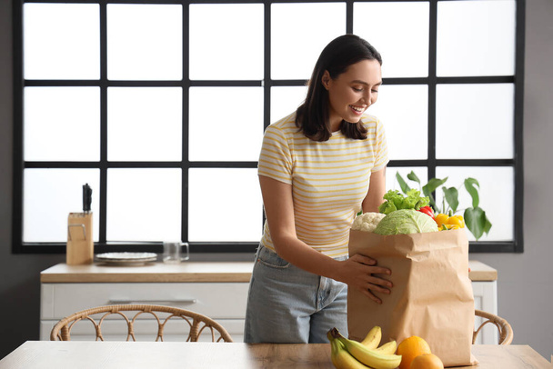 Молодая женщина с бумажным пакетом здоровой пищи на кухне - Фото, изображение