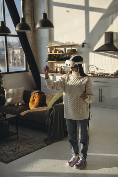 Eine junge Frau, die in ein Online-Spiel vertieft ist, trägt zu Hause ein Virtual-Reality-Headset. Hochwertiges Foto - Foto, Bild