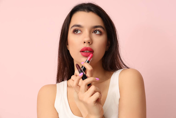 Hermosa mujer joven con lápices labiales con estilo sobre fondo rosa - Foto, imagen