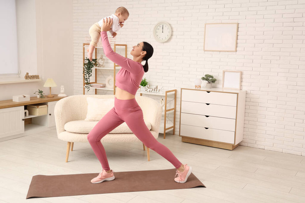 自宅でヨガを練習する彼女の小さな赤ちゃんと美しい若いスポーティな女性 - 写真・画像