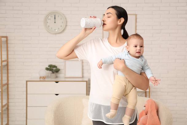 Beautiful young sporty woman drinking water and holding her little baby at home - Photo, Image