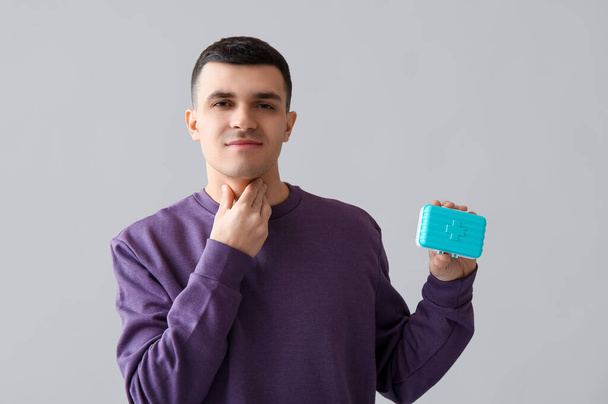Nuori mies, jolla on kilpirauhanen ongelma ja pilleri laatikko kevyellä taustalla - Valokuva, kuva