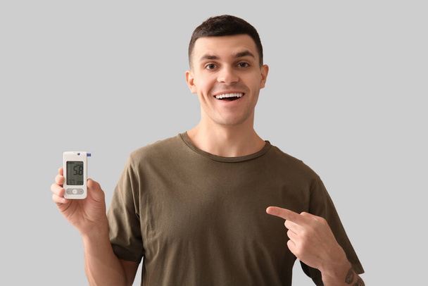 Діабетичний молодий чоловік вказує на глюкометр на світлому фоні - Фото, зображення