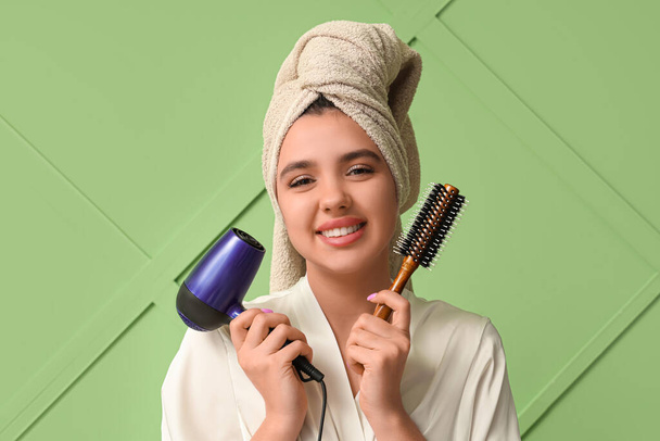 Όμορφη νεαρή ευτυχισμένη γυναίκα με στεγνωτήρα μαλλιών και πινέλο στο πράσινο φόντο - Φωτογραφία, εικόνα